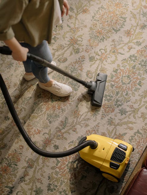 A person operating a yellow industrial extractor or vacuum cleaner, designed for deep cleaning surfaces, on a beige and cream patterned carpet with hints of green and orange, situated in a well-lit ro